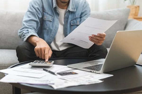 A man at his kitchen table working through a stack of bills with a calculator
