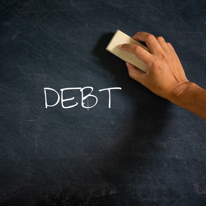 A hand erasing the word DEBT from a chalkboard